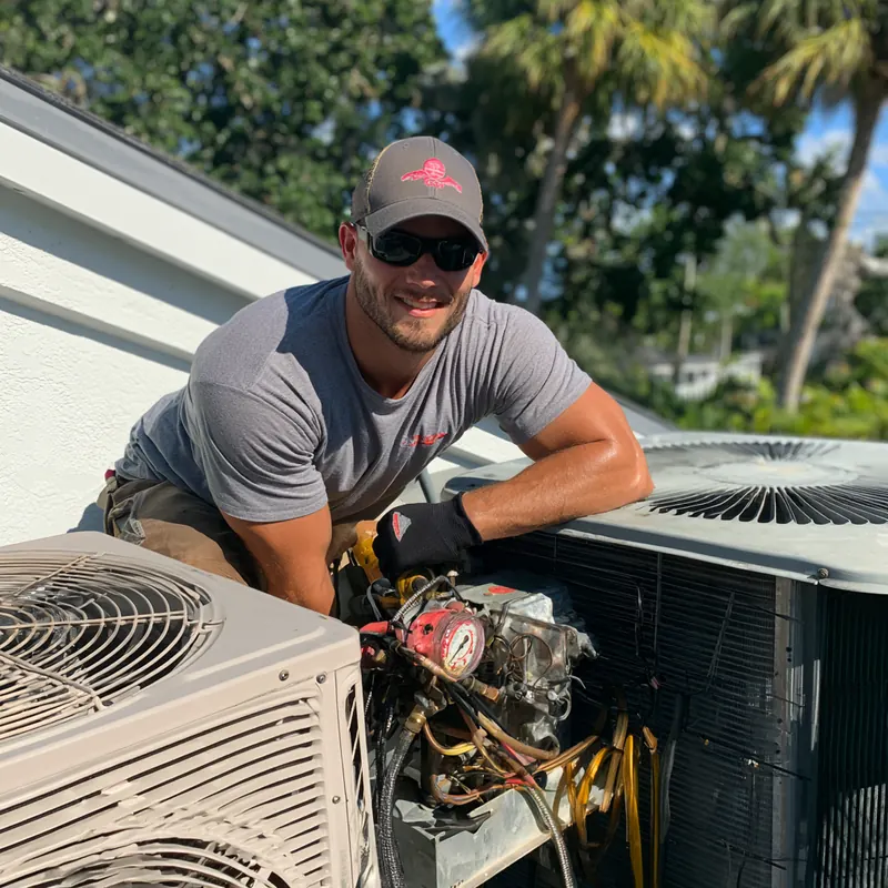 Smiling technician with service gauges leaning between two outdoor air conditioning units