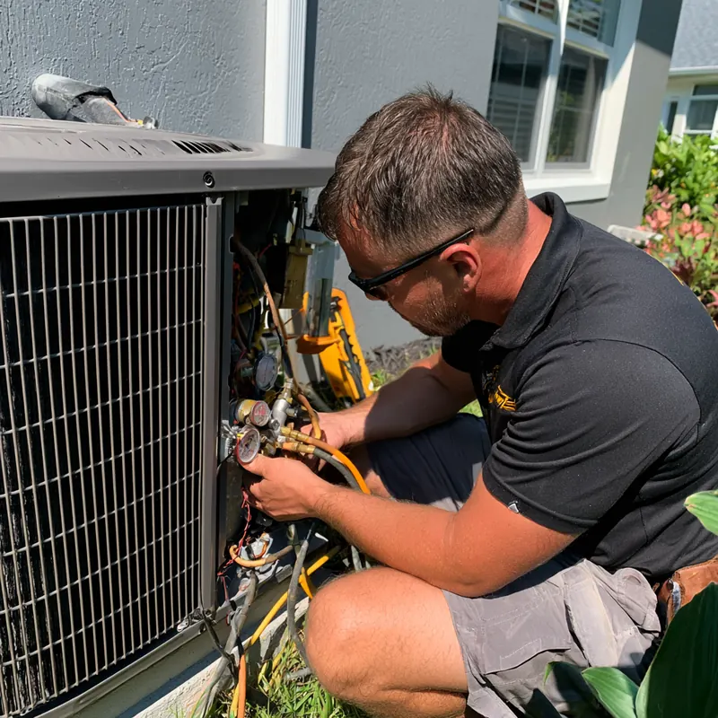 Technician in safety glasses reading manifold gauges connected to an outdoor air conditioner